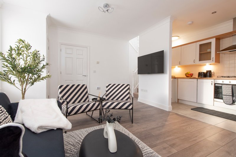 Open-plan living area with striped accent chairs, TV, kitchen, and modern furnishings