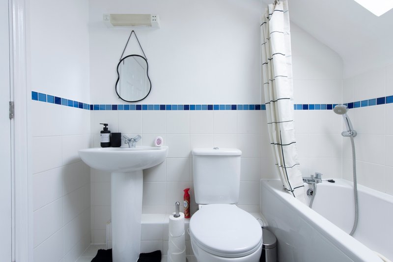 Clean bathroom with pedestal sink, toilet, bathtub and blue tile accent strip