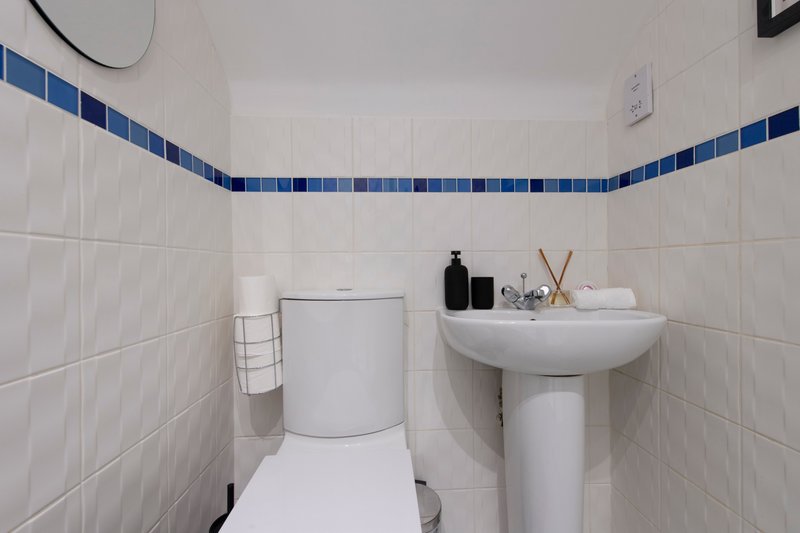 Small bathroom with toilet, pedestal sink, white tile walls and blue tile trim