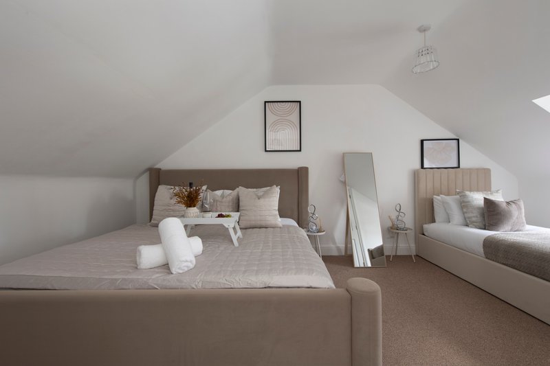 Bright attic bedroom with two beds, neutral bedding, and minimalist wall decor