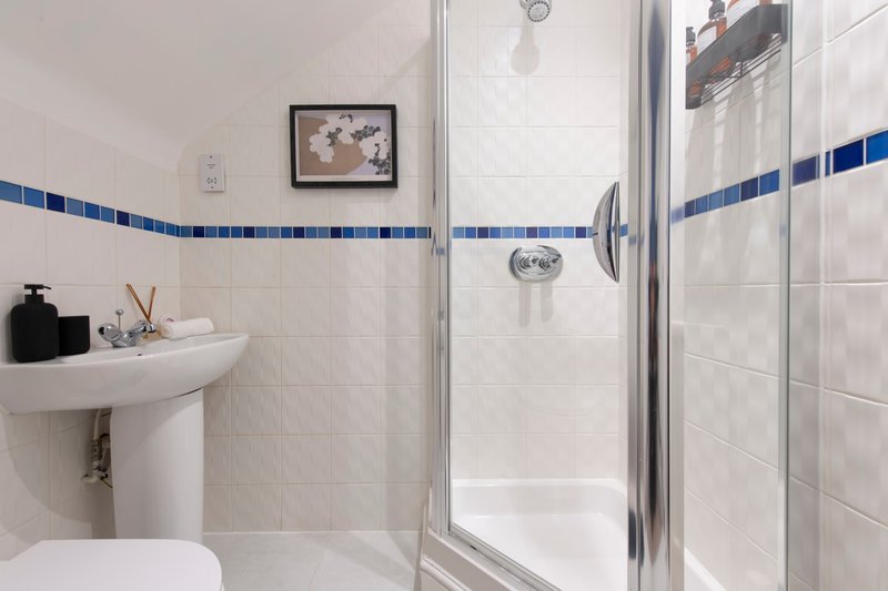 Modern bathroom with white tiles, blue border stripe, shower cubicle and pedestal sink