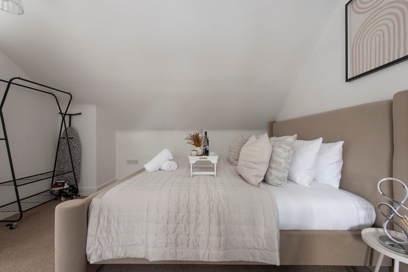 Bright bedroom with beige upholstered bed, white pillows, neutral bedding, and sloped ceiling