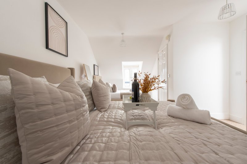 Bright modern bedroom with neutral bedding, pillows, wine bottle and dried flowers on bed