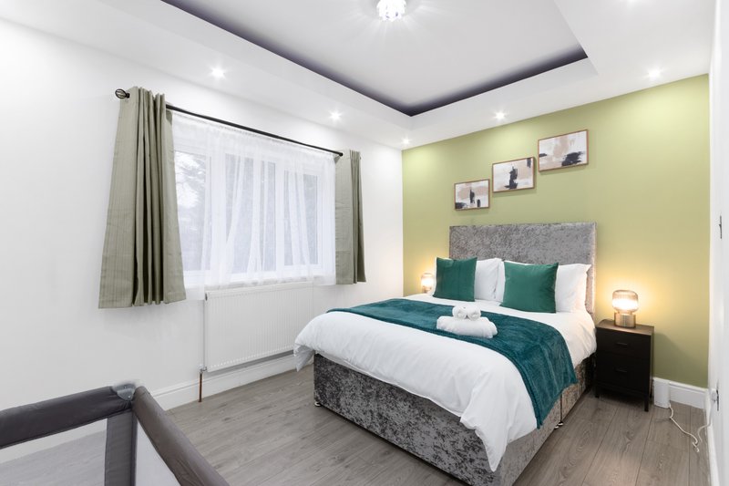 Modern bedroom with double bed, green accent wall, window with curtains and bedside lamps