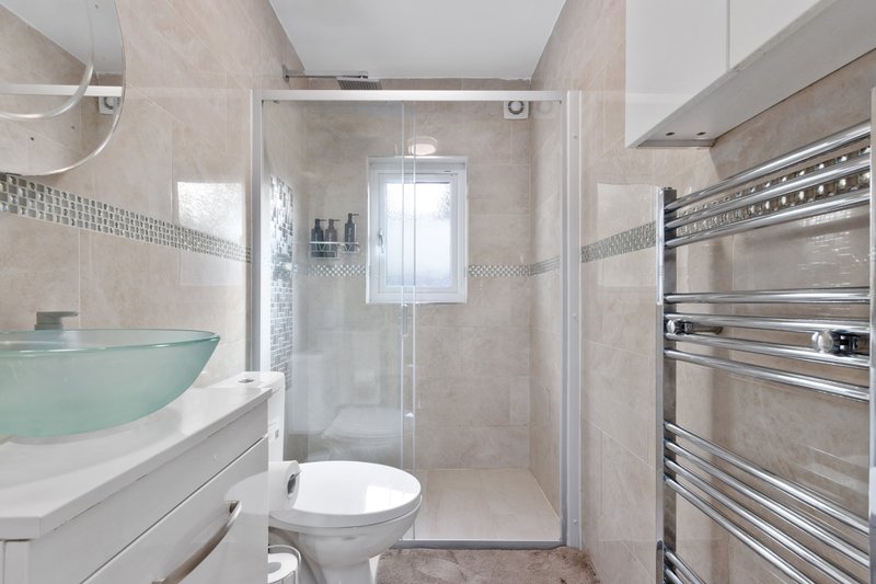Modern bathroom with glass shower enclosure, toilet, vanity sink and heated towel rail