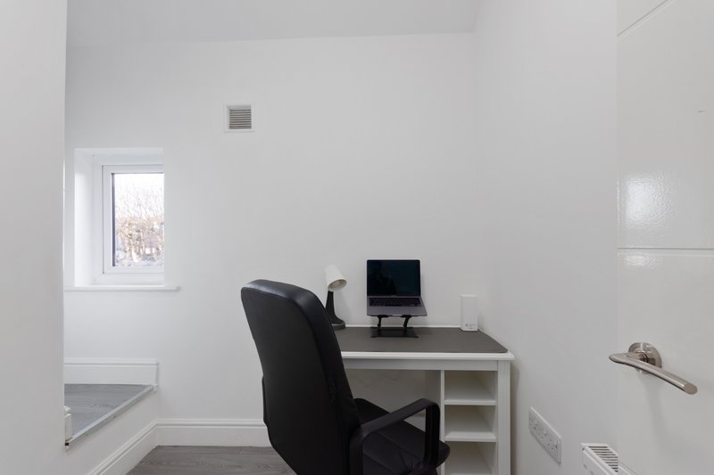 Minimalist home office with white desk, black chair, laptop, and window with natural light