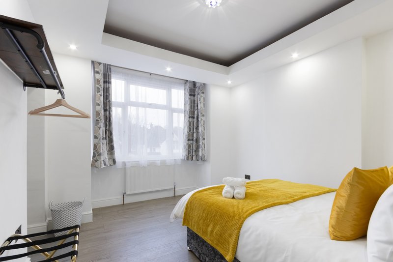 Modern bedroom with double bed, yellow bedding, window with curtains and wooden floor