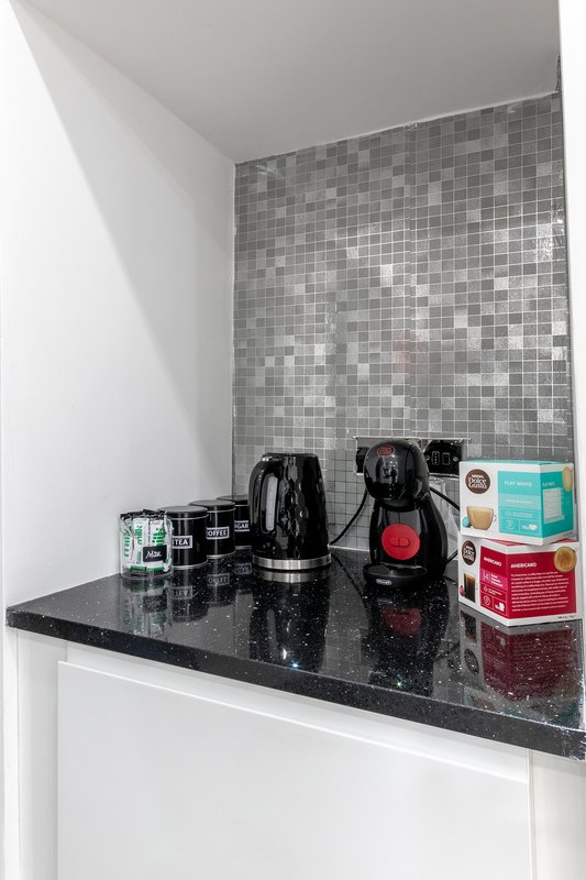 Kitchen counter with kettle, coffee maker, and various packaged items against tiled backsplash
