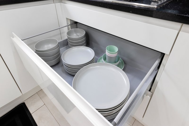 Open kitchen drawer displaying white plates, bowls, and green-rimmed dishes neatly stacked