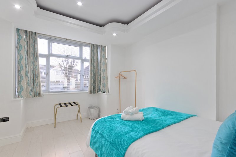 Bright modern bedroom with white walls, turquoise bedding, wooden coat stand and large window