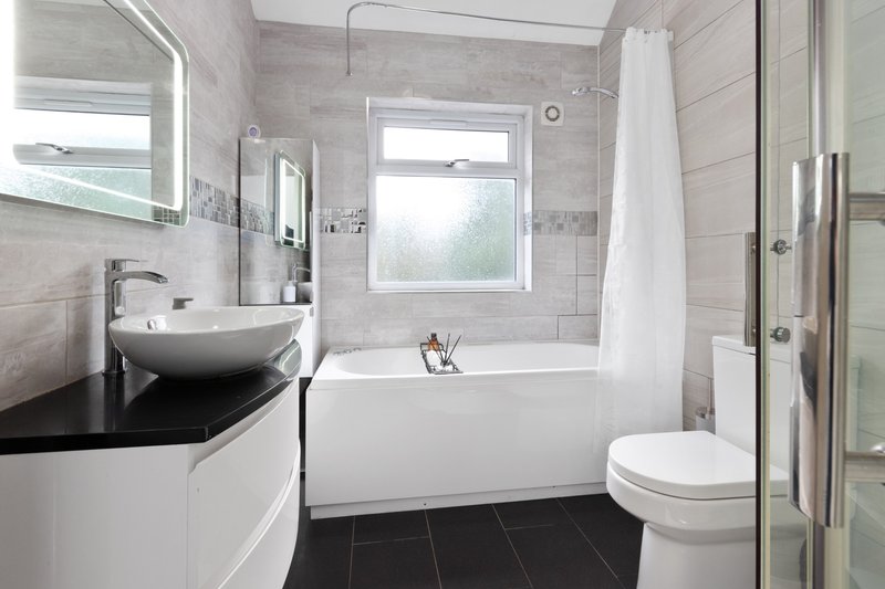 Modern bathroom with white basin sink, bathtub, toilet, and black tile flooring