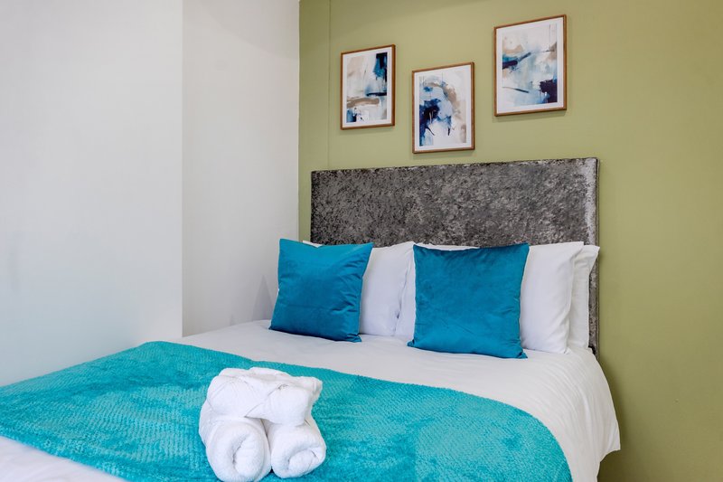 Modern bedroom with double bed, grey headboard, turquoise bedding and blue cushions