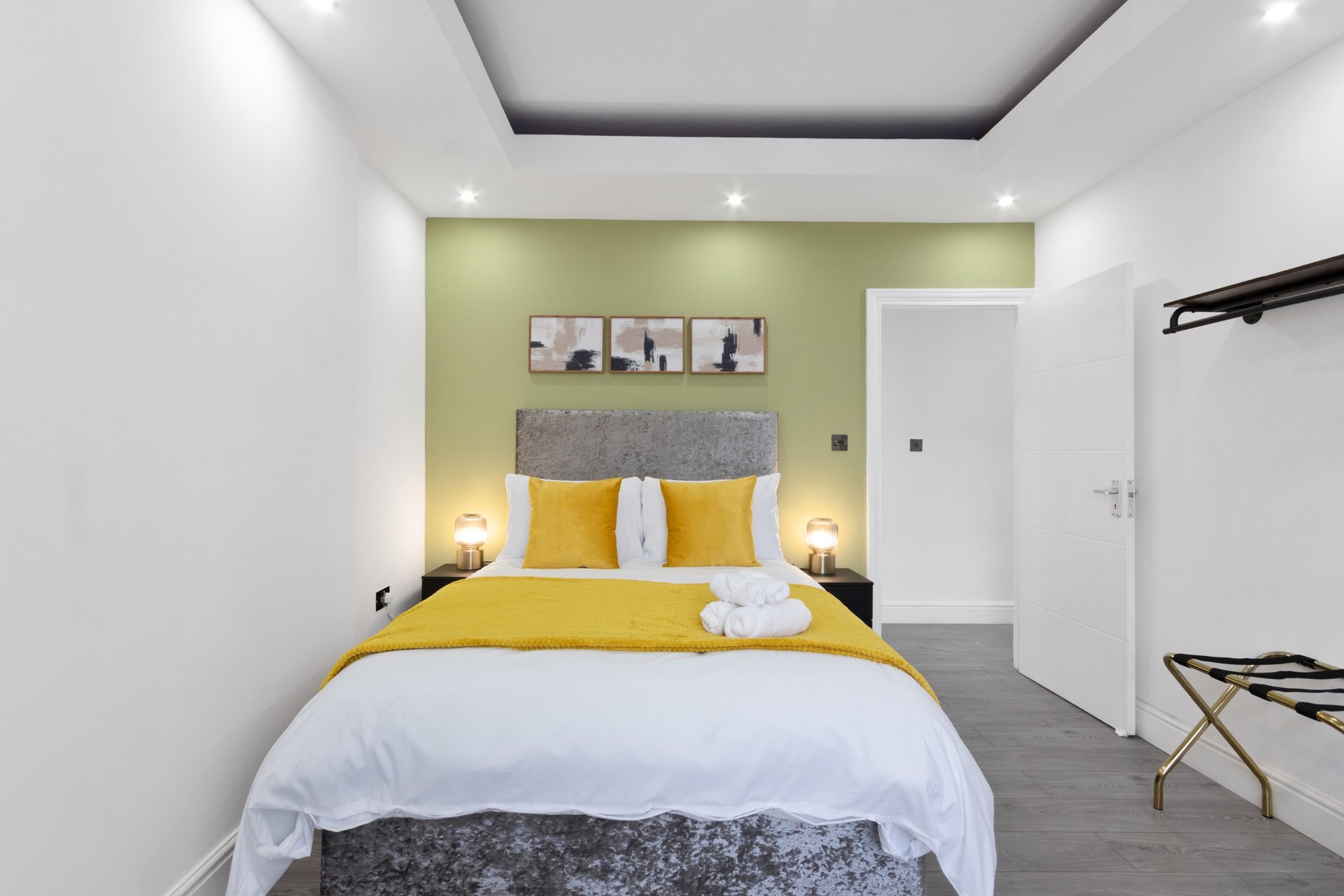 Modern bedroom with yellow accent wall, double bed with yellow bedding, grey headboard, and pendant lighting