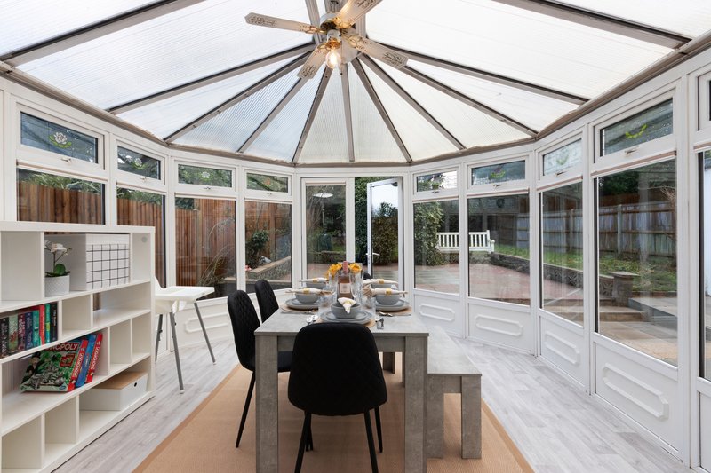 Bright conservatory with dining table, black chairs, built-in shelving and garden views