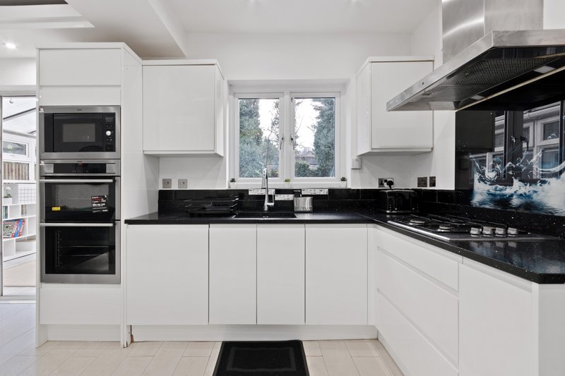 Modern white kitchen with black countertops, built-in appliances, and garden view windows