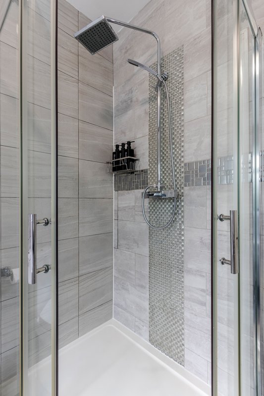 Modern bathroom shower enclosure with rainfall showerhead, grey tile walls and white base