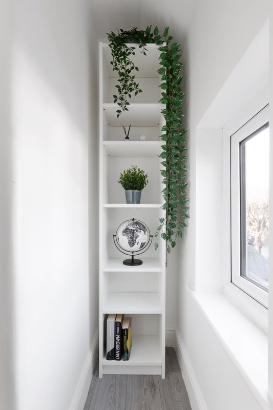 Narrow hallway with tall white shelving unit displaying plants, globe, and decorative items