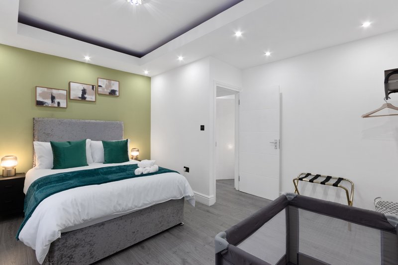 Modern bedroom with double bed, green accent wall, white ceiling, and recessed lighting