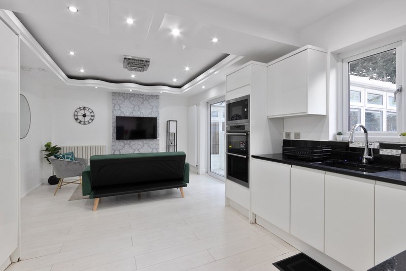 Modern open-plan kitchen and living room with white cabinetry, black countertop, green sofa and wall-mounted TV