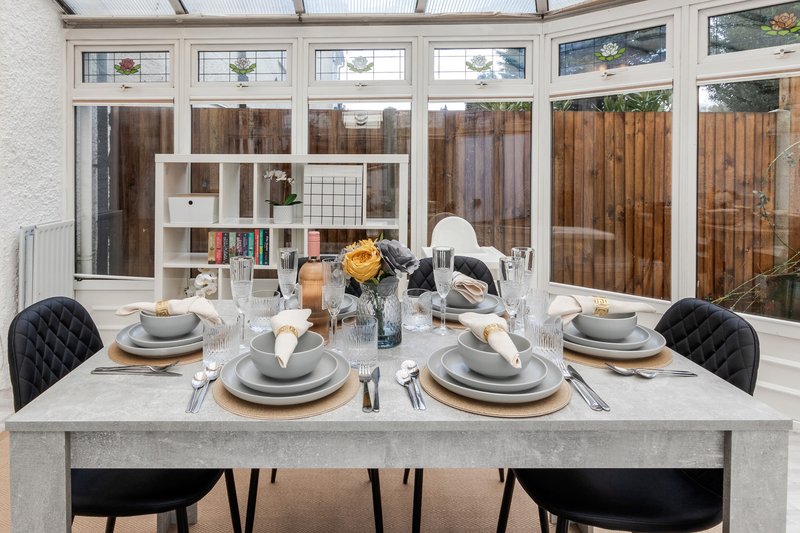 Modern dining table set for four with place settings, black chairs, and garden view through windows