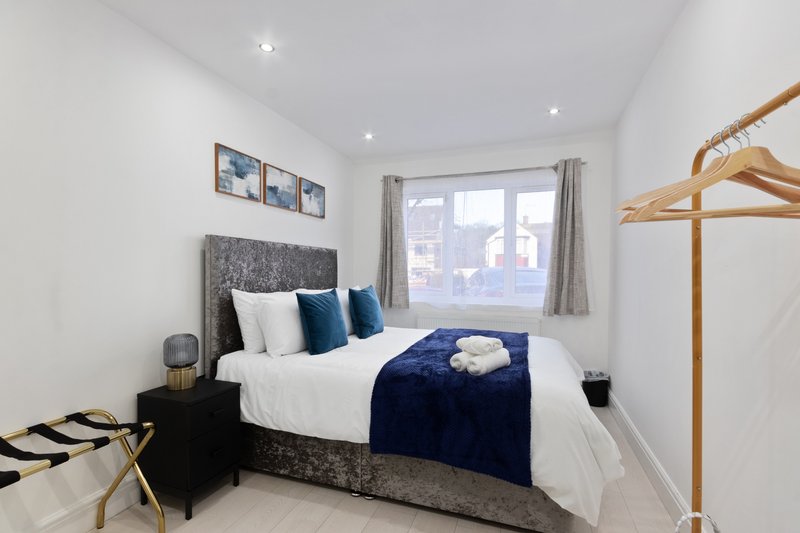 Bright modern bedroom with double bed, grey headboard, blue throw, wooden coat stand and window