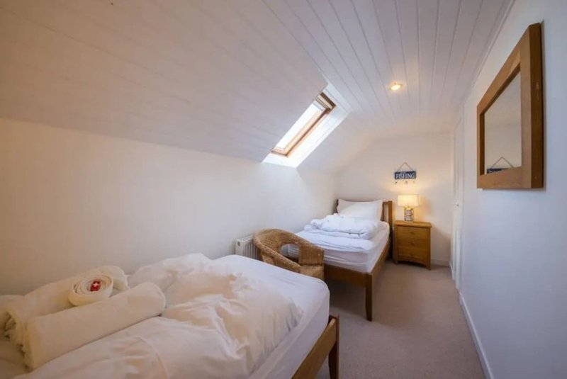 Attic bedroom with two single beds, wooden furniture, skylight and wall mirror