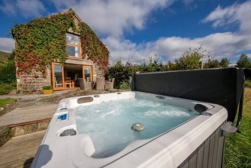Stone cottage with ivy-covered walls, wooden deck, and hot tub in foreground