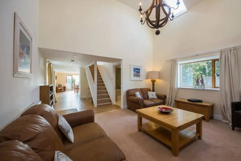 Spacious living room with brown leather sofa, wooden coffee table, and staircase to upper floor