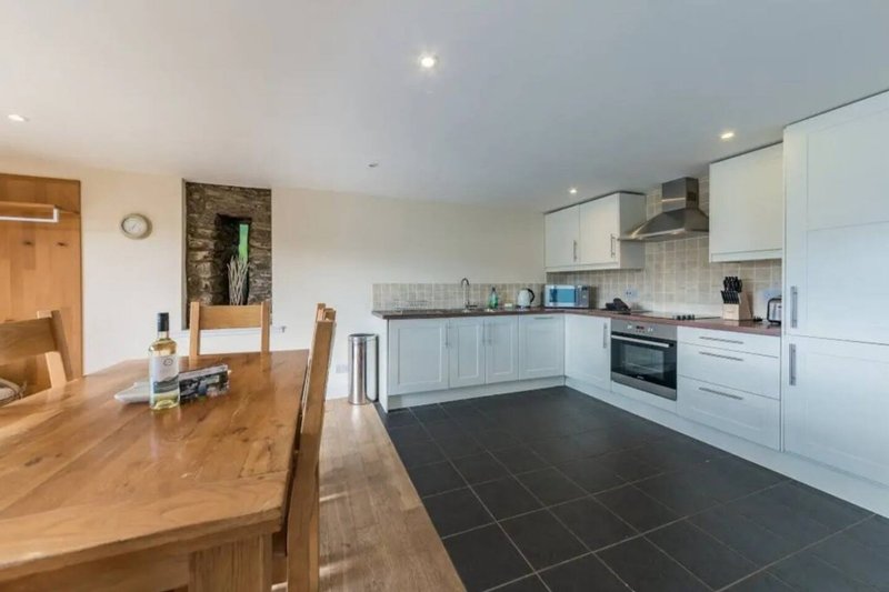 Open-plan kitchen and dining area with white cabinetry, wooden table, and black tile flooring