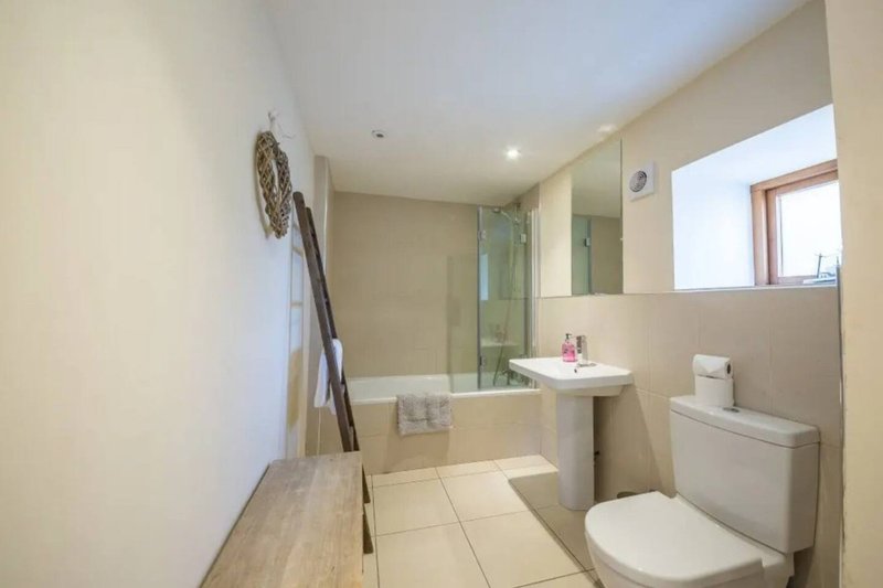 Modern bathroom with toilet, pedestal sink, shower enclosure and beige tile flooring