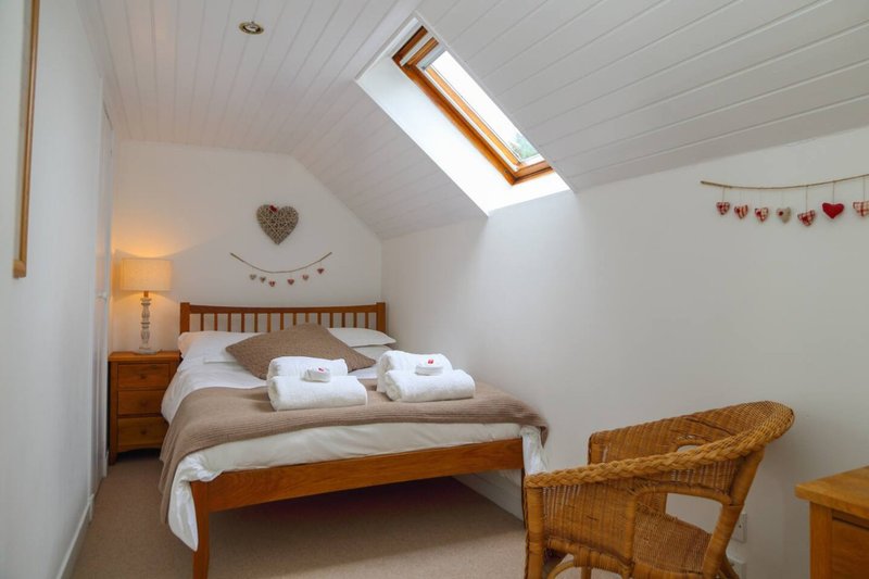 Attic bedroom with wooden bed, white bedding, wicker chair and skylight window