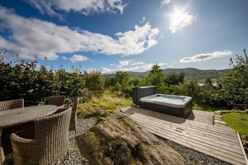 Elevated wooden deck with hot tub, dining table and mountain views