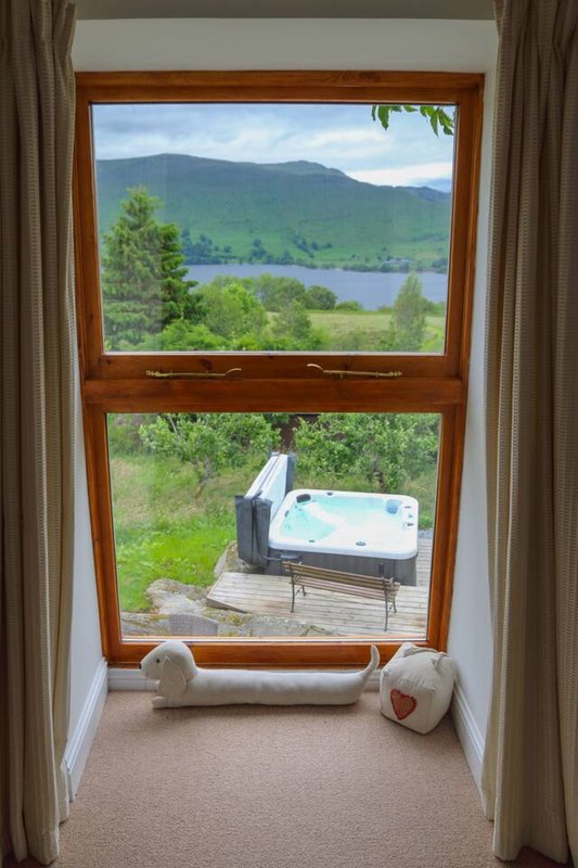 Window view of lake and mountains with hot tub visible on deck below