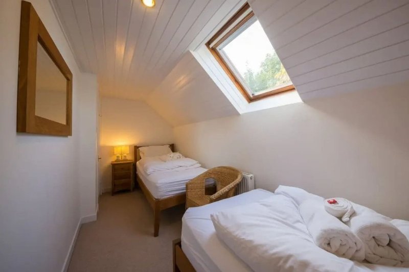 Attic bedroom with two single beds, skylight window, wooden furniture and neutral decor