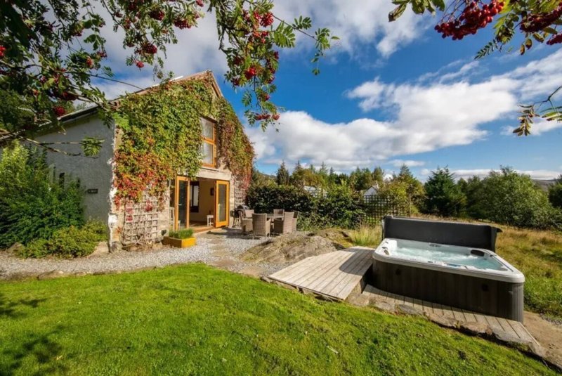 Stone cottage with garden, hot tub, and countryside views under blue sky