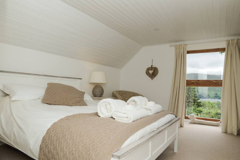 Bright bedroom with double bed, white bedding, beige throws, and countryside view through window
