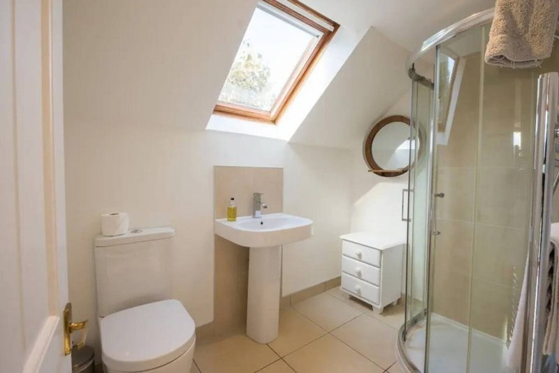 Bright bathroom with skylight, toilet, pedestal sink, shower cubicle and circular mirror