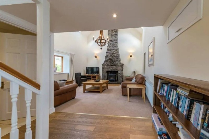 Open-plan living room with stone fireplace, leather sofa, wooden furniture and bookshelves