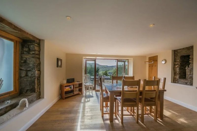 Open-plan living and dining room with wooden floors, stone fireplace, and countryside views through glass doors