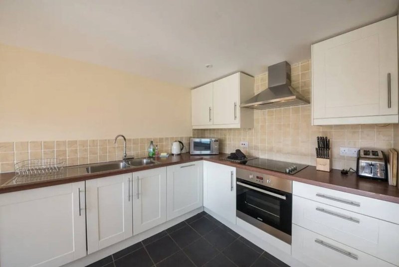 Modern kitchen with white cabinets, black countertops, built-in oven and cream tile backsplash