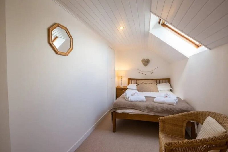 Attic bedroom with wooden bed, white bedding, skylights and wicker chair