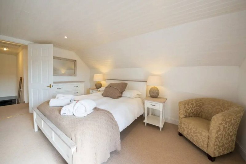 Bright bedroom with double bed, white bedding, two lamps, armchair and ensuite door