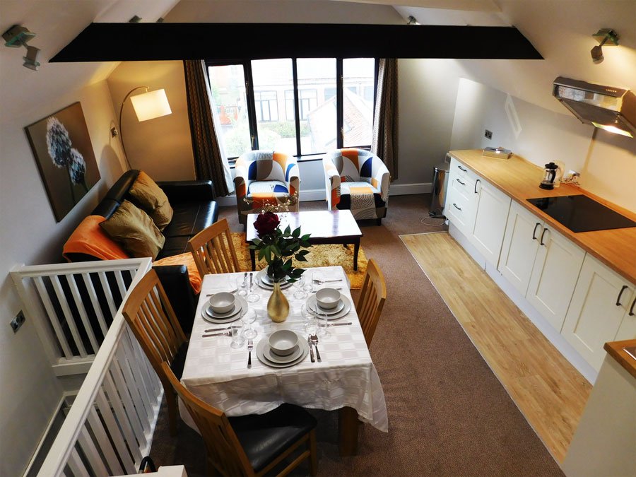 Open-plan studio with dining table, kitchen area, sofa and two chairs by windows