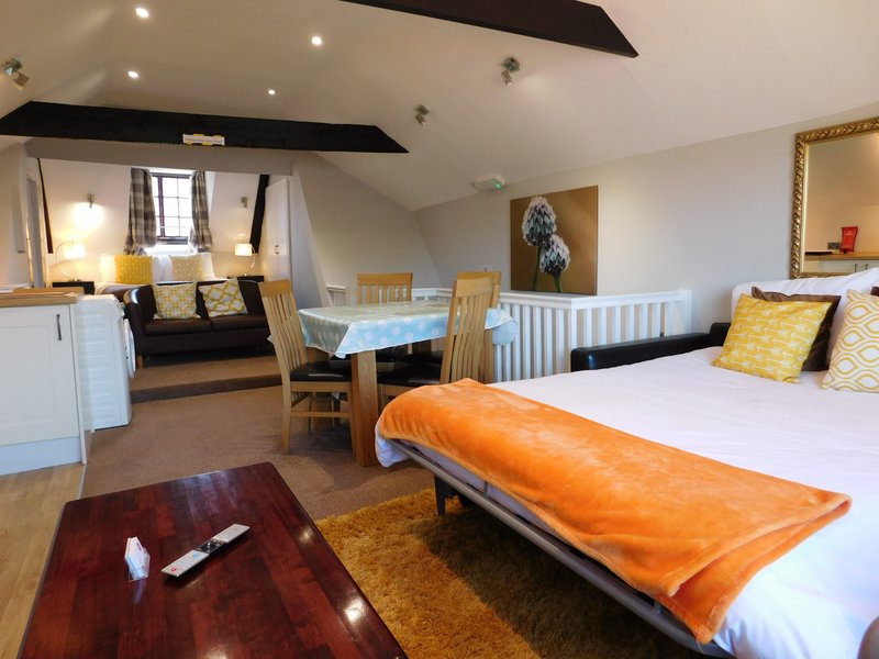 Open-plan bedroom and living area with double bed, dining table, kitchen, and black beam ceiling