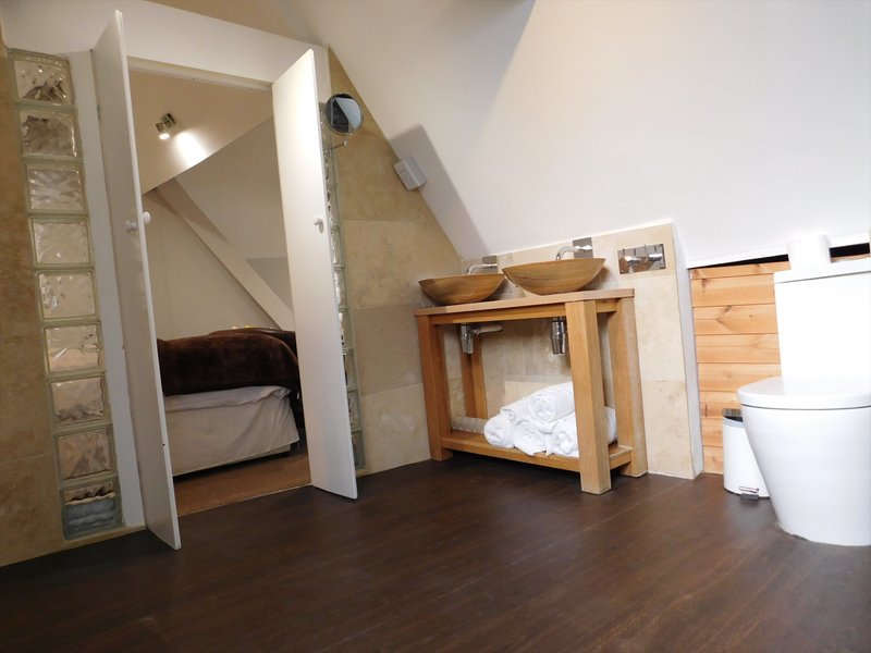 Attic bedroom with sloped ceiling, two beds, wooden furniture and dark flooring