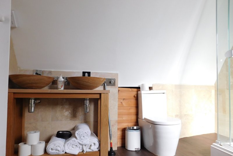 Bathroom with wooden vanity, white toilet, rolled towels, and bright natural light from window