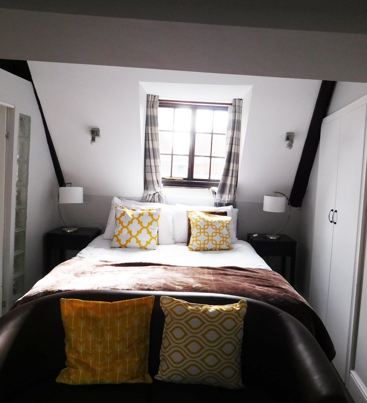 Modern bedroom with double bed, yellow patterned cushions, skylight window and bedside lamps