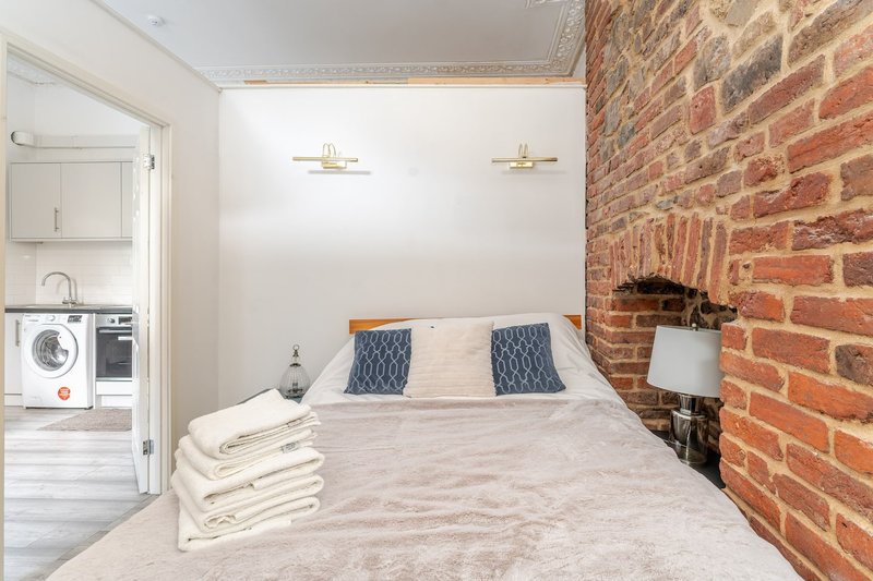 Bedroom with double bed, brick accent wall, folded towels, and open-plan kitchen visible