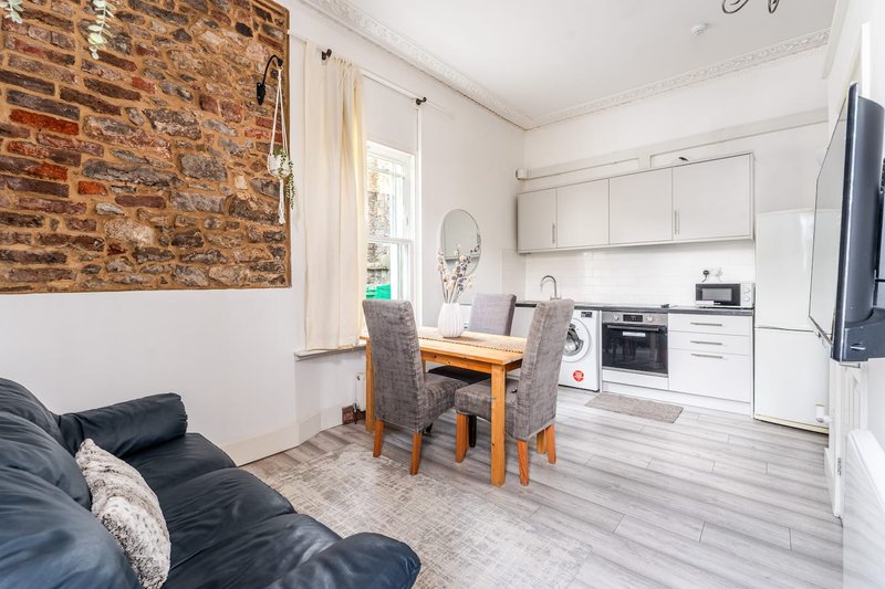 Open-plan living and kitchen space with brick accent wall, dining table, black sofa and white cabinetry