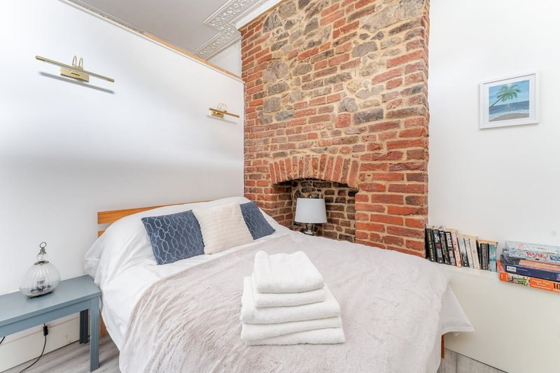 Cozy bedroom with double bed, exposed brick chimney breast, and wooden shelving